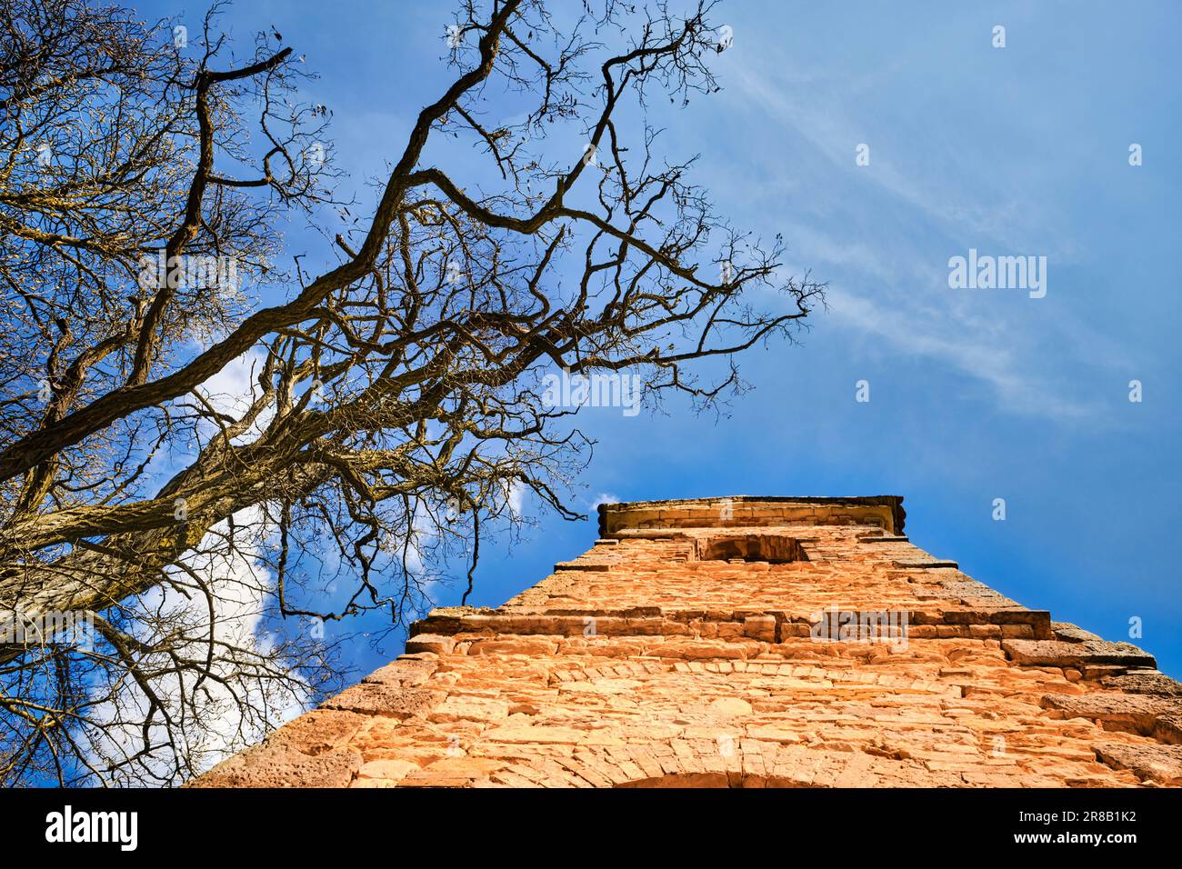 Rovine di un'antica chiesa abbandonata campanile in pietra e di un albero secco sotto un cielo blu in una giornata di sole. Testimone del decadimento rurale. Foto Stock