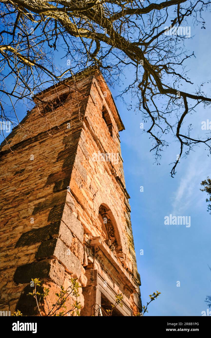 Rovine di un'antica chiesa abbandonata campanile in pietra e di un albero secco sotto un cielo blu in una giornata di sole. Testimone del decadimento rurale. Foto Stock