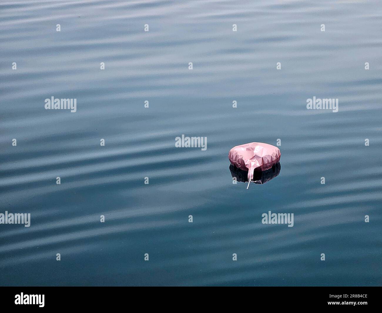 Palloncino con cuore rosa sgonfio che galleggia sull'acqua blu del lago Foto Stock