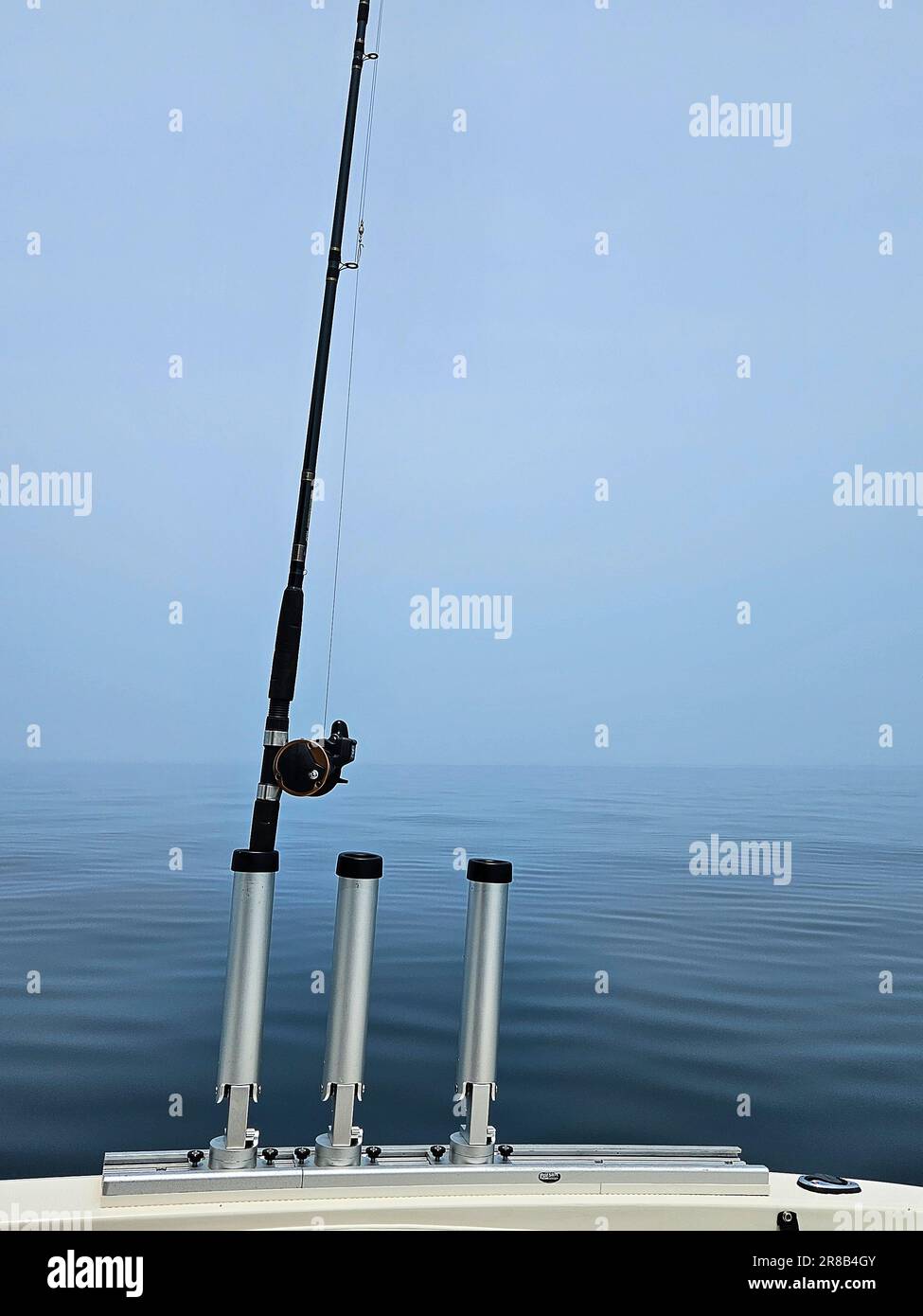 Supporti verticali per canne da pesca con canna su una barca con cielo nebbioso e fondo blu Foto Stock