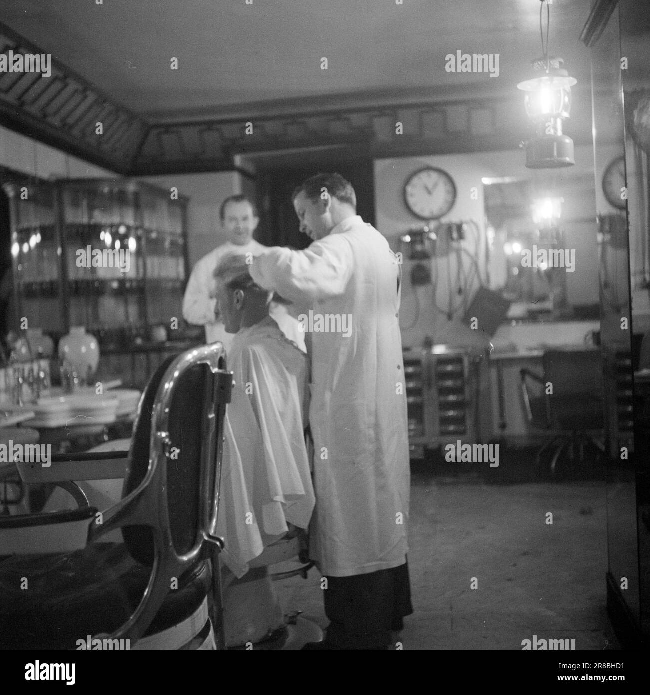 Corrente 22-1-1947: Il passato in un'ora di visitoPer un'ora ogni mattina, l'elettricità viene spenta a Oslo, come tanti altri luoghi del paese. A Oslo, il tempo di disconnessione è 11,30–12,30, in altri luoghi ci possono essere altri tempi. – L'interruzione dell'alimentazione provoca una significativa interruzione del lavoro per le aziende che dipendono dall'elettricità per le loro macchine. Cecil Barbersalong si trova su un piano seminterrato, ma la luce viene risparmiata grazie a numerose potenti lampade a cherosene. Tuttavia, i rasaerba elettrici devono essere azionati manualmente tra 11,30 e 12,30. Foto: TH. Skotaam / Aktuell / NTB Foto Stock