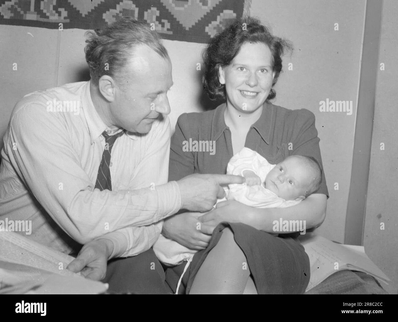 Attuale 18-1947: Avamposto norvegese di Svalbardnell'Oceano Artico attualmente in visita a Longyearbyen a Svalbard e dando ai lettori un assaggio di vita come minatore o trapper. Svalbard è amministrata come un'entità indipendente sotto un governatore, che è il più alto funzionario norvegese dell'arcipelago. Il governatore si chiama Håkon Balstad. Qui lo troviamo nell'angolo del divano insieme a sua moglie Liv e al figlio di un mese Stein Balstad, nipote dell'autore. Vesle Stein è il primo bambino nato a Longyearbyen dopo la guerra. Sembra che si stia godendo. Foto: TH. Skotaam / Aktuell / NTB Foto Stock