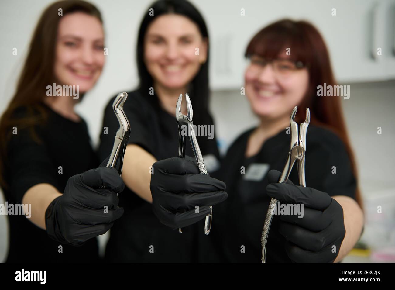 Pinze dentali in acciaio inox, pinze per estrarre i denti in mani guantate di squadra offuscata di dentisti femminili medici Foto Stock