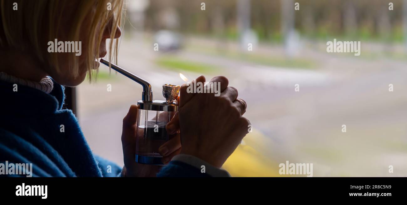 Una donna accende un bong di marijuana. Dispositivo per il fumo di cannabis. Un mezzo di rilassamento, concentrazione. Foto Stock