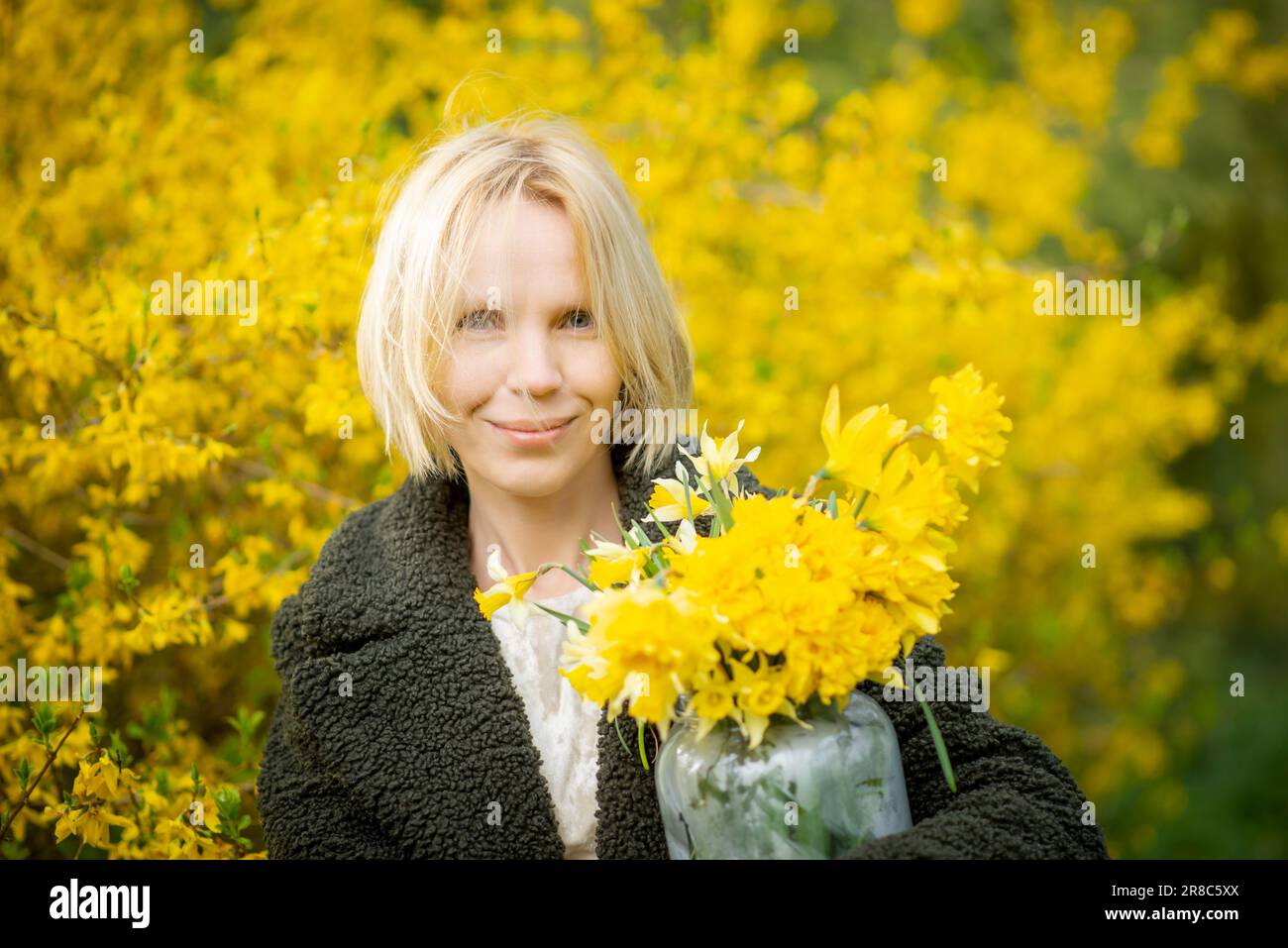 Donna su sfondo giallo con fiori gialli. Donna bionda di mezza età sorridente più di quaranta anni. Faccia felice, pensieri leggeri, sogni. Foto Stock