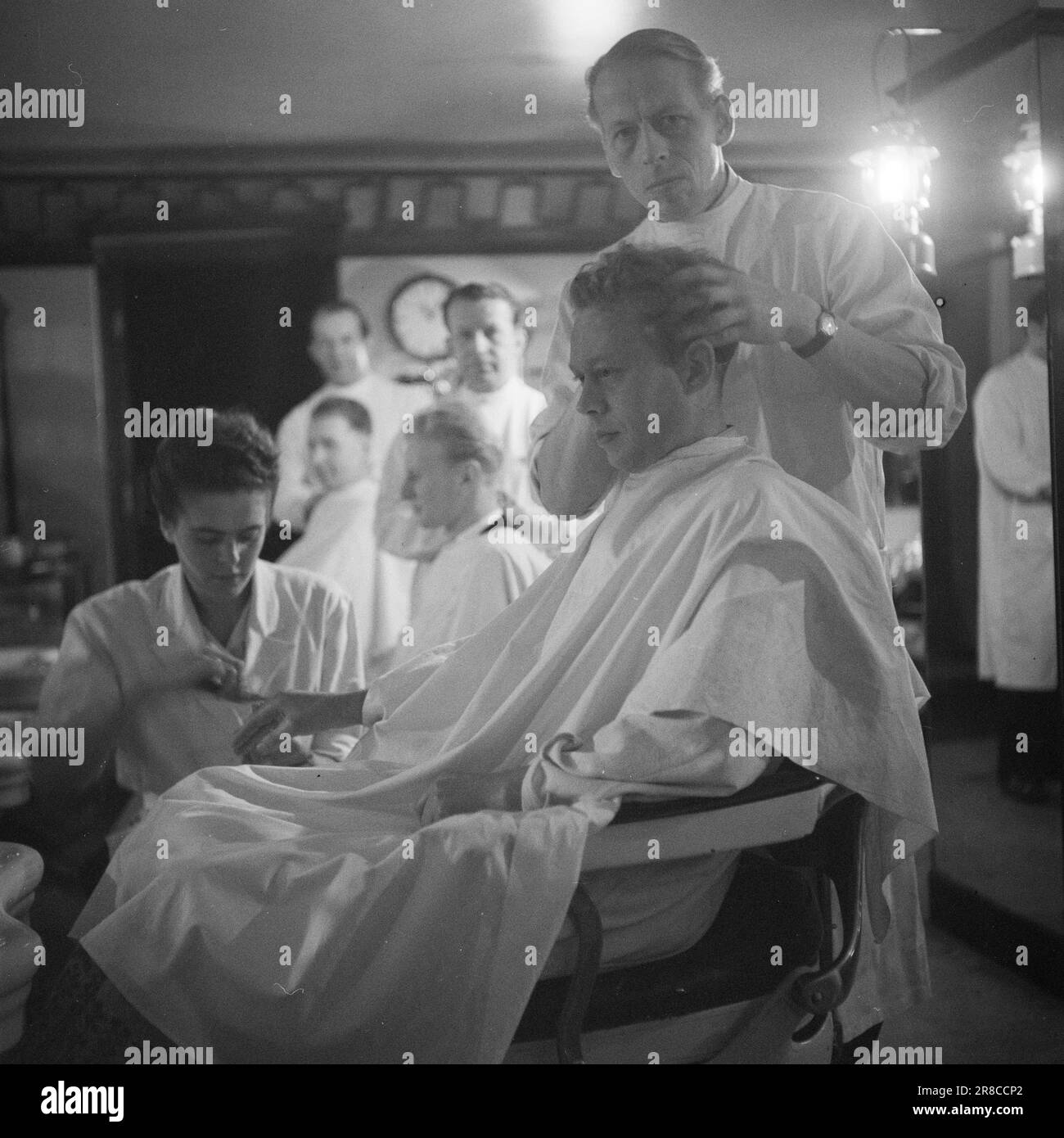 Corrente 22-1-1947: Il passato in un'ora di visitoPer un'ora ogni mattina, l'elettricità viene spenta a Oslo, come tanti altri luoghi del paese. A Oslo, il tempo di disconnessione è 11,30–12,30, in altri luoghi ci possono essere altri tempi. – L'interruzione dell'alimentazione provoca una significativa interruzione del lavoro per le aziende che dipendono dall'elettricità per le loro macchine. Cecil Barbersalong si trova su un piano seminterrato, ma la luce viene risparmiata grazie a numerose potenti lampade a cherosene. Tuttavia, i rasaerba elettrici devono essere azionati manualmente tra 11,30 e 12,30. Foto: TH. Skotaam / Aktuell / NTB Foto Stock