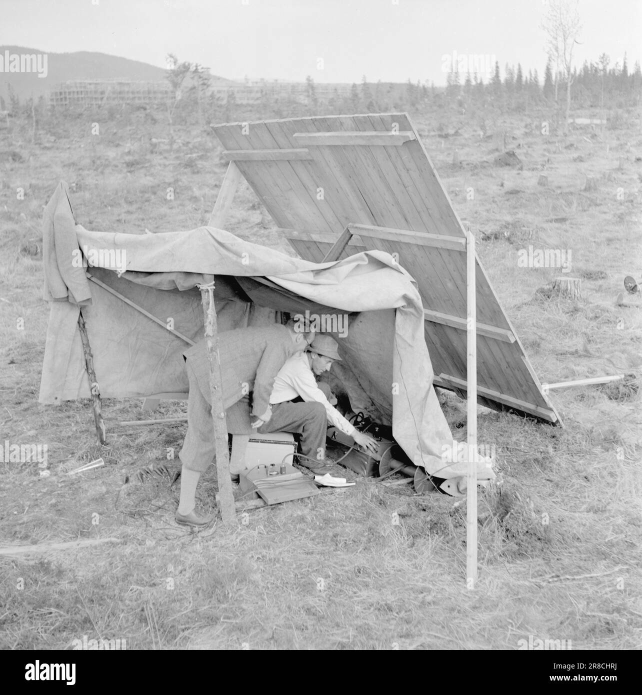 Corrente 14-1950: Jernverket in Mo i Rana.Well oltre 800 uomini sono in procinto di erigere le opere di ferro in Mo i Rana, e il lavoro sta progredendo rapidamente. I colpi di mine in piena espansione, l'ossigeno che batte dalle perforatrici a compressione e le masse rocciose massicce l'aria per tremare e fremere, e giù nella montagna i tunnel incrociano la loro strada. Molto è stato fatto, ma molto resta ancora da fare. Gli ingegneri svedesi Hasselström e Fagerlund effettuano misurazioni a terra con il geofono. Il dispositivo non solo misura la profondità della roccia solida, ma registra anche gli strati di suolo. Foto: Sverre A. Børretzen / Aktu Foto Stock