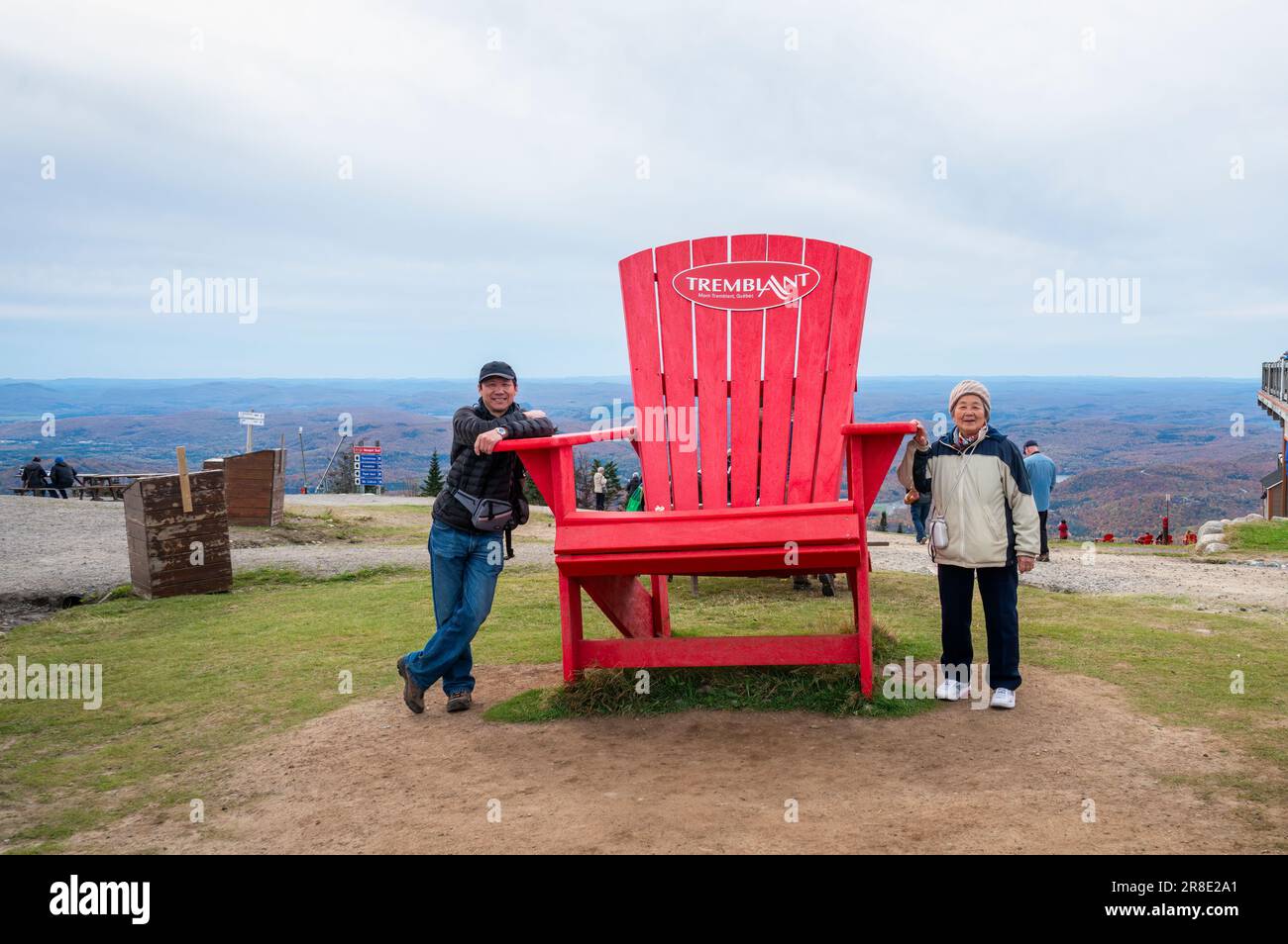 Donna e figlio cinese anziano in posa per le foto da gigantesca sedia rossa alla cima del Mont Tremblant. Quebec. Canada. Foto Stock