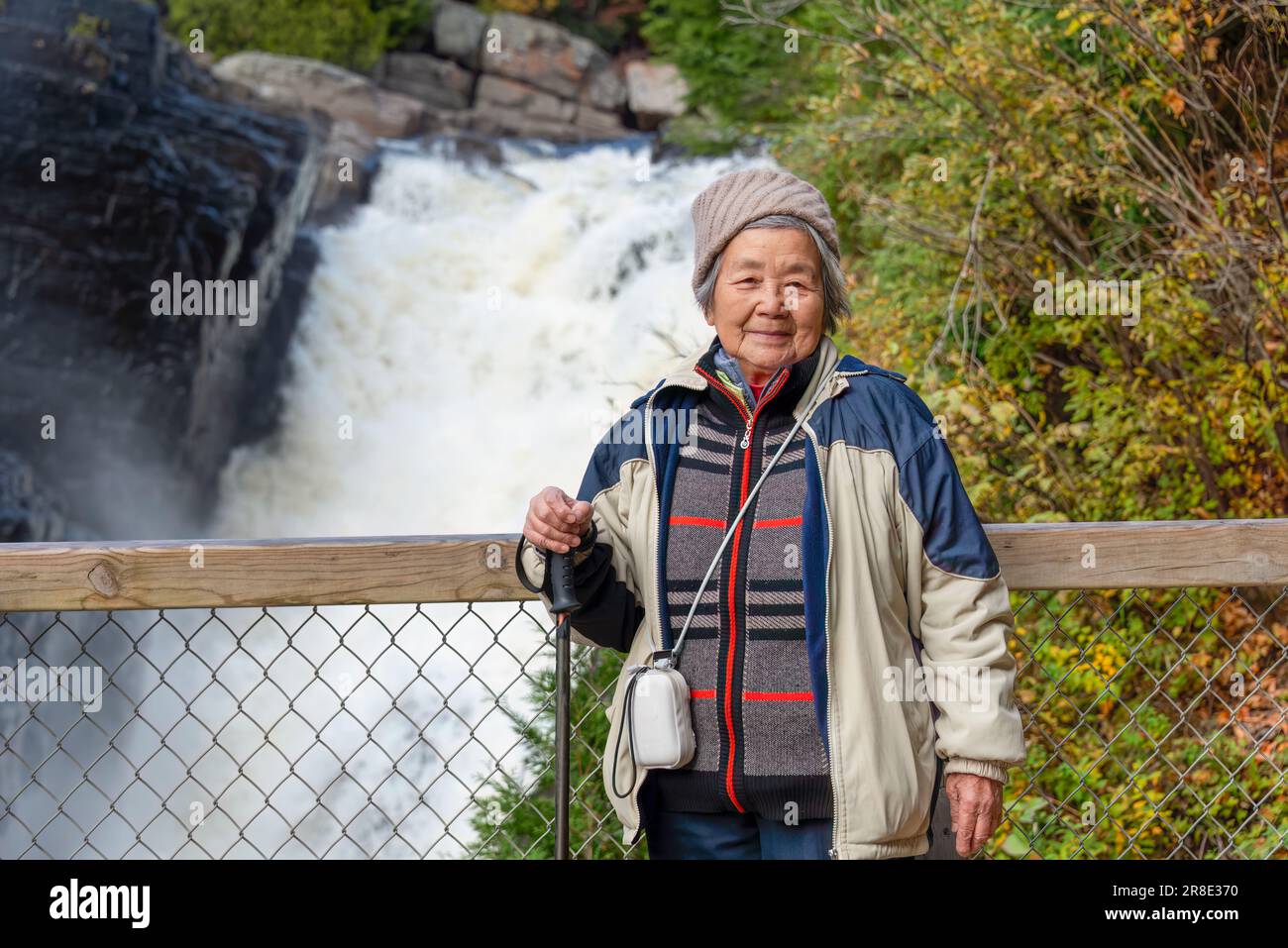 Turista cinese anziano in posa per le foto di fronte alle cascate al Canyon Sainte-Anne. Quebec in autunno. Canada. Foto Stock