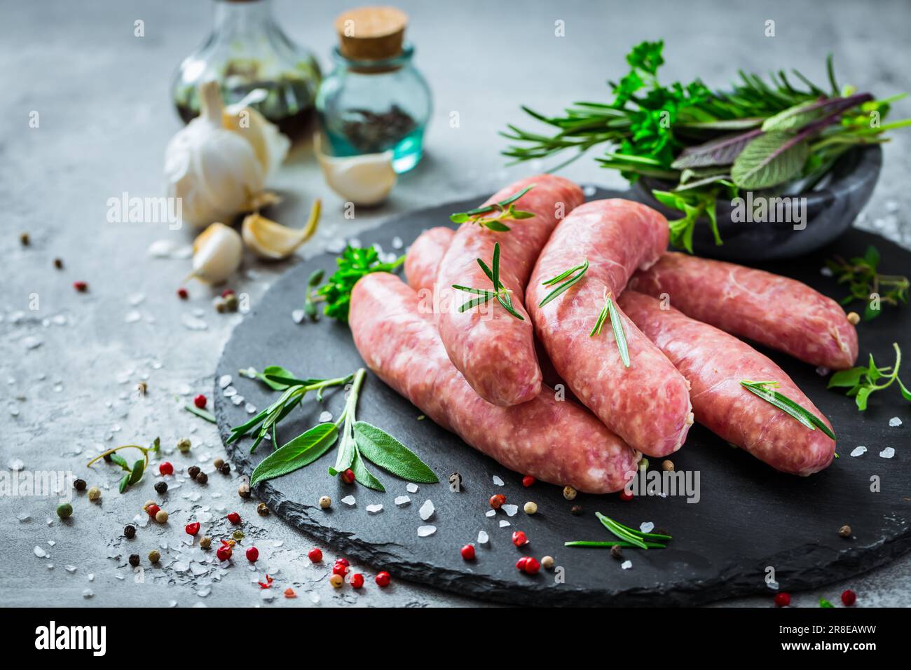 Salsicce crude su ardesia, con erbe e spezie, preparate per grigliate e barbecue Foto Stock