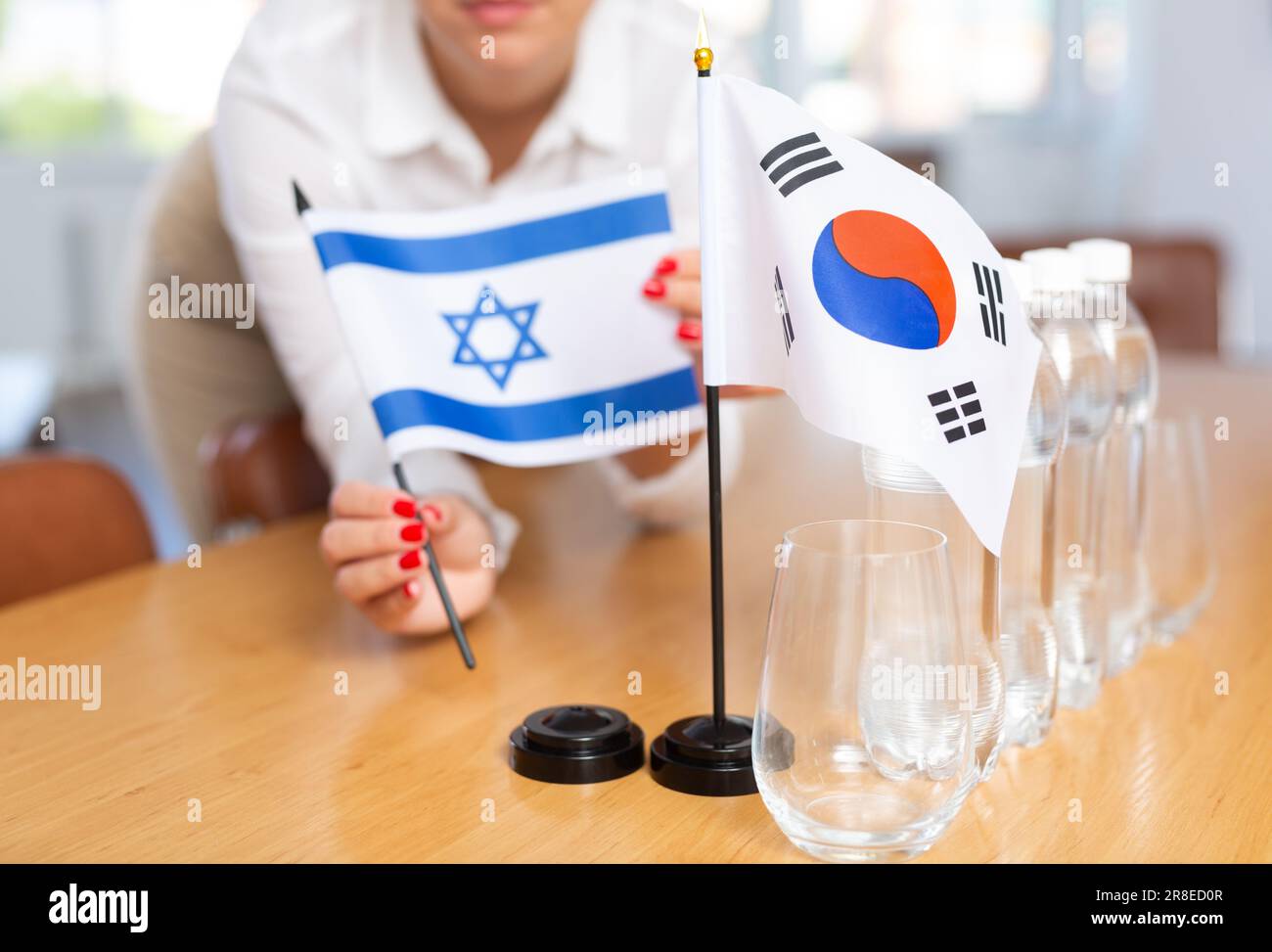 Mani femminili che mettono bandiere della Corea del Sud e di Israele sul tavolo negoziale Foto Stock