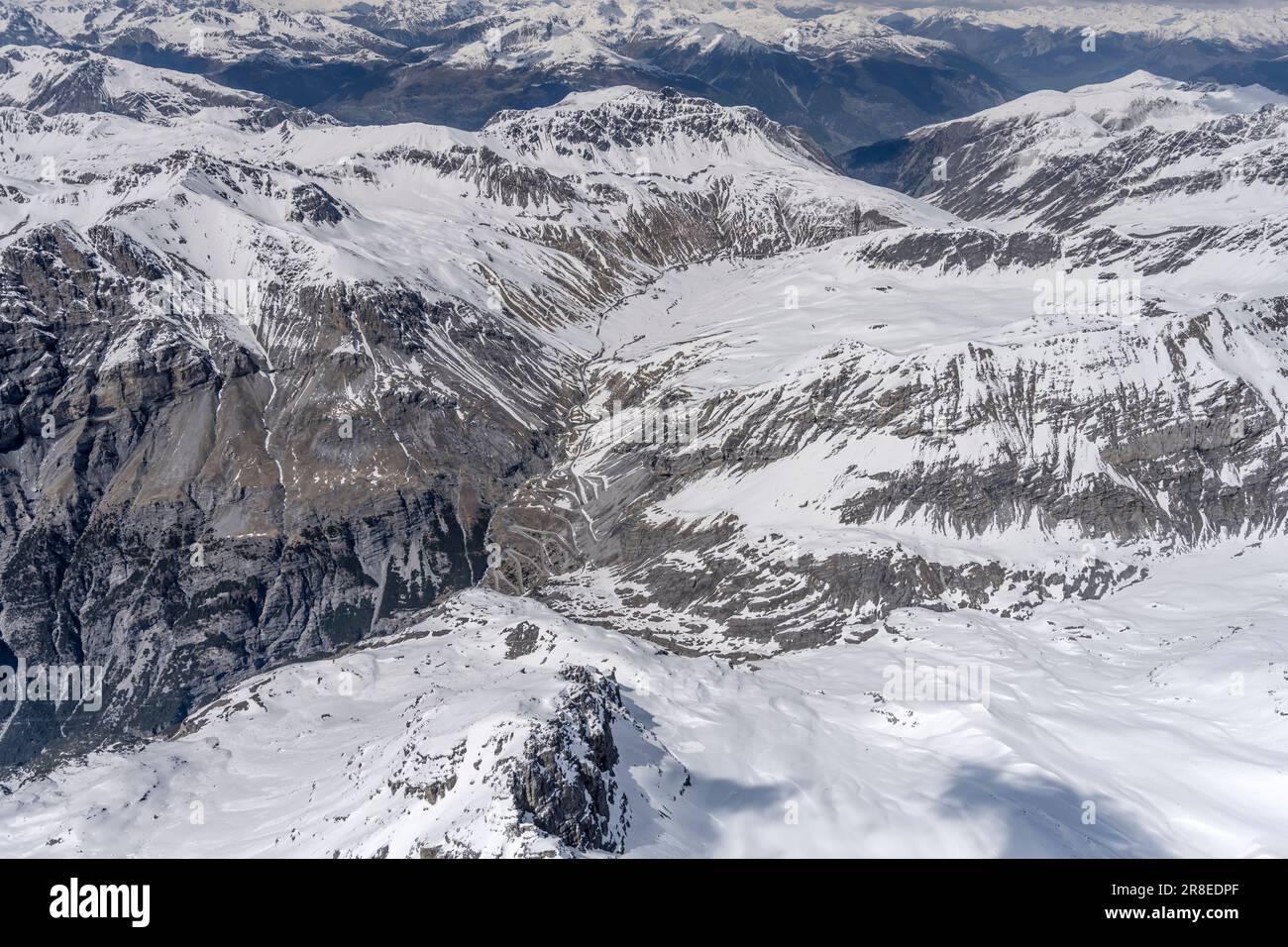 Paesaggio aereo, da un velivolo, di tornanti al passo dello Stelvio tra pendii rocciosi innevati, sparati da sud-ovest in luminosa Lig tardo primaverile Foto Stock