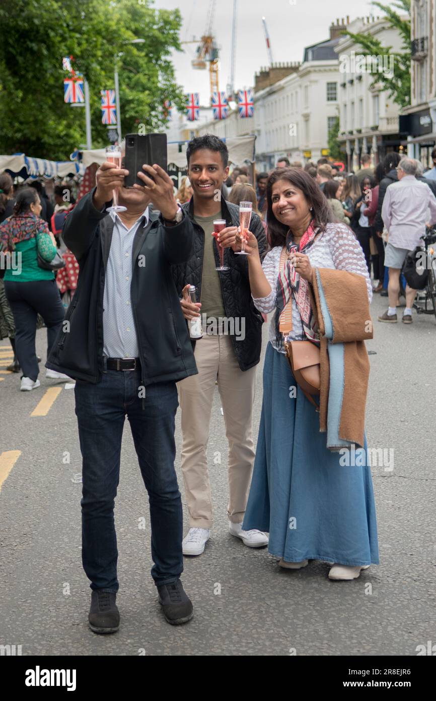 Gruppo di famiglie asiatiche nel Regno Unito, scatta un selfie con occhiali da picnic in plastica con champagne. The Kings Road, Platinum Jubilee Street Party. Chelsea, Londra, Inghilterra 4 giugno 2022. HOMER SYKES anni '2020 Foto Stock
