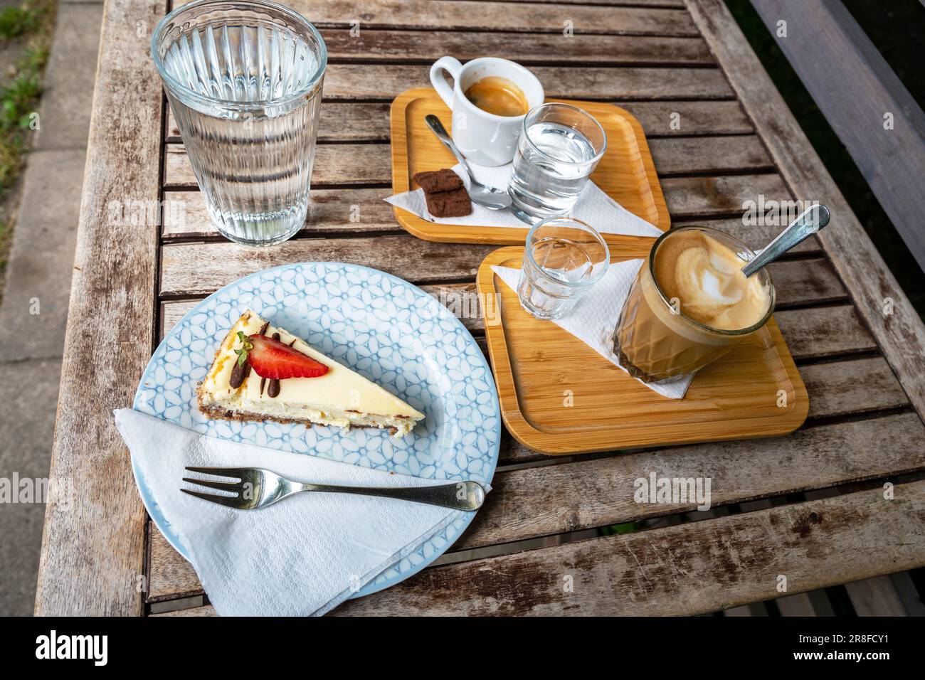 Cheesecake, due caffè e acqua su piccolo vassoio su tavolo in legno in giardino. Foto Stock