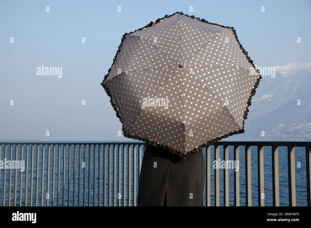 Donna che appoggia su una ringhiera sul lungomare con un ombrello Foto Stock