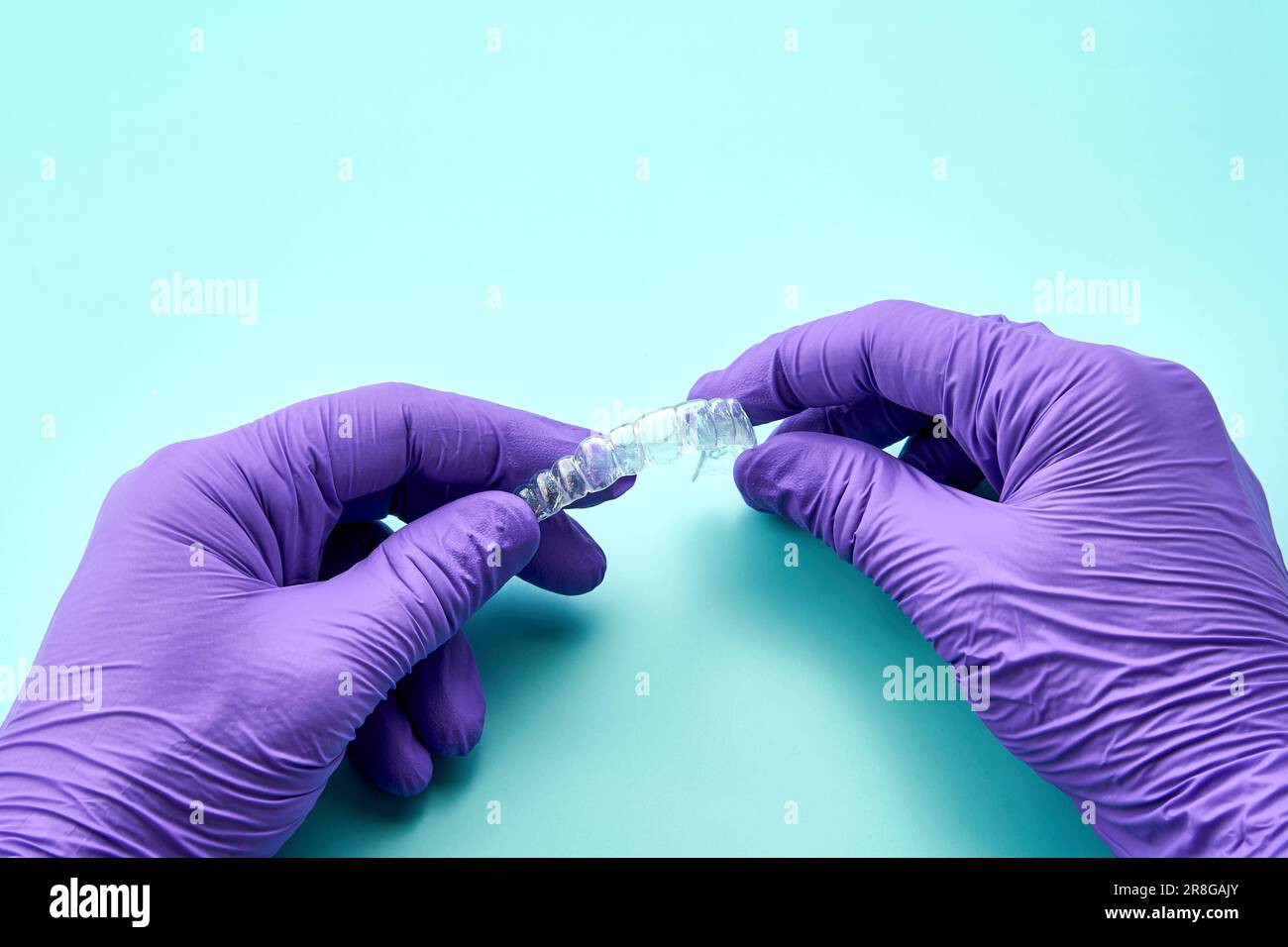 Tecnico odontoiatrico con bretella invisibile in laboratorio odontoiatrico, indossando guanti viola e un tavolo verde. Foto Stock