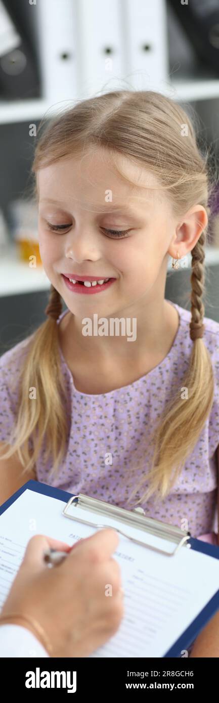 Amichevole medico pediatra donna che tiene appunti ascoltando la bambina Foto Stock