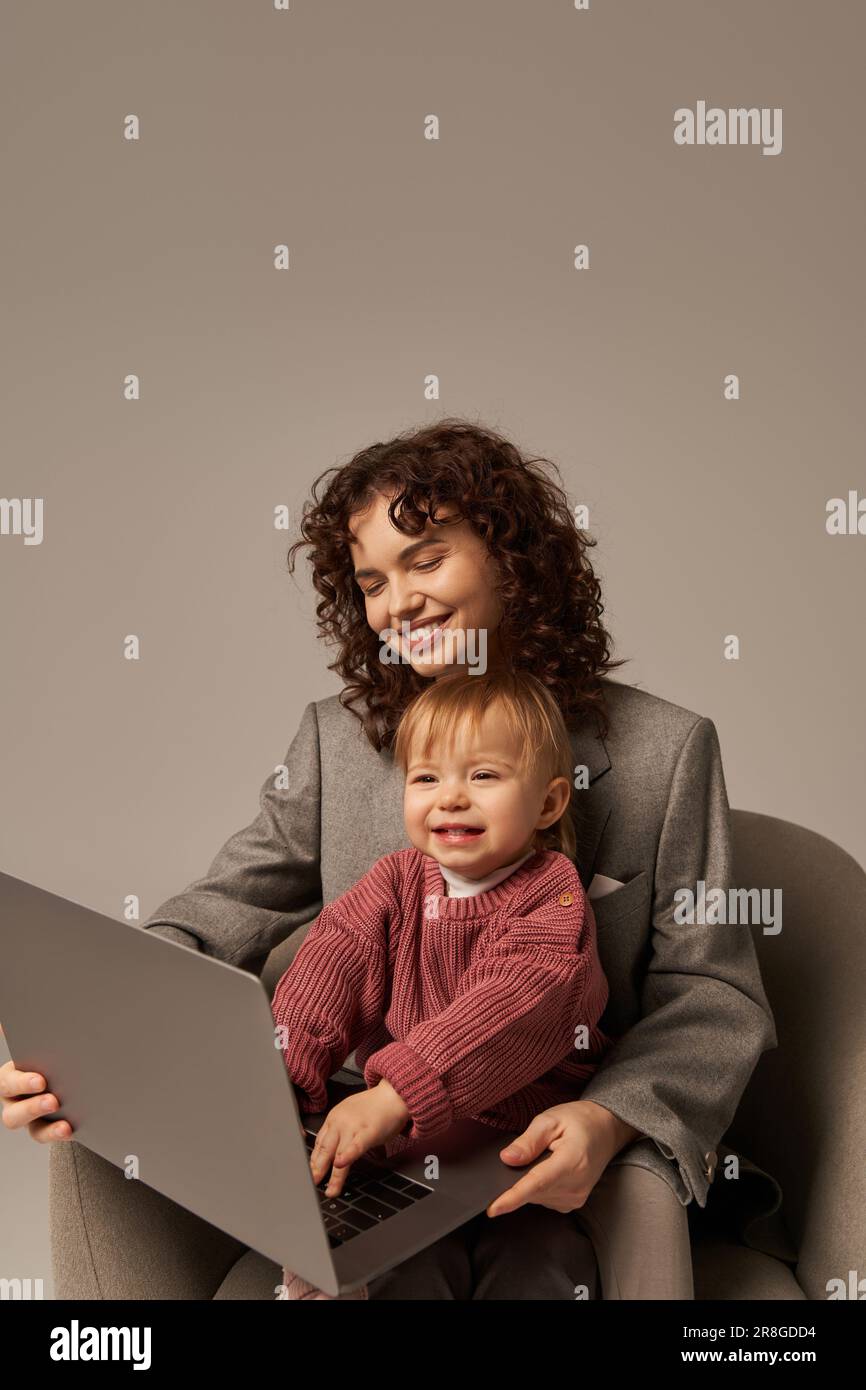 costruire una carriera di successo, uno stile di vita equilibrato, un genitore che lavora, una donna allegra che usa il notebook e che si siede in poltrona con figlia, madre e bambino Foto Stock