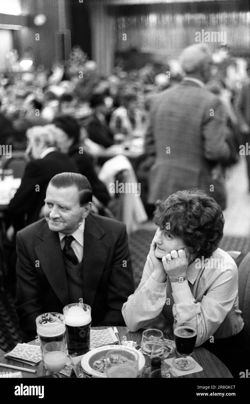Coppia che beve insieme sabato sera fuori. Anni '1980 Regno Unito. Le loro carte da bingo sono sul tavolo. Sono un grande posacenere metallico. Indossa i suoi vestiti, abiti e cravatte migliori e ha dorso brylCreamed e lucidato i suoi capelli ha una parte laterale molto bassa. Coventry, Inghilterra 1981. HOMER SYKES Foto Stock