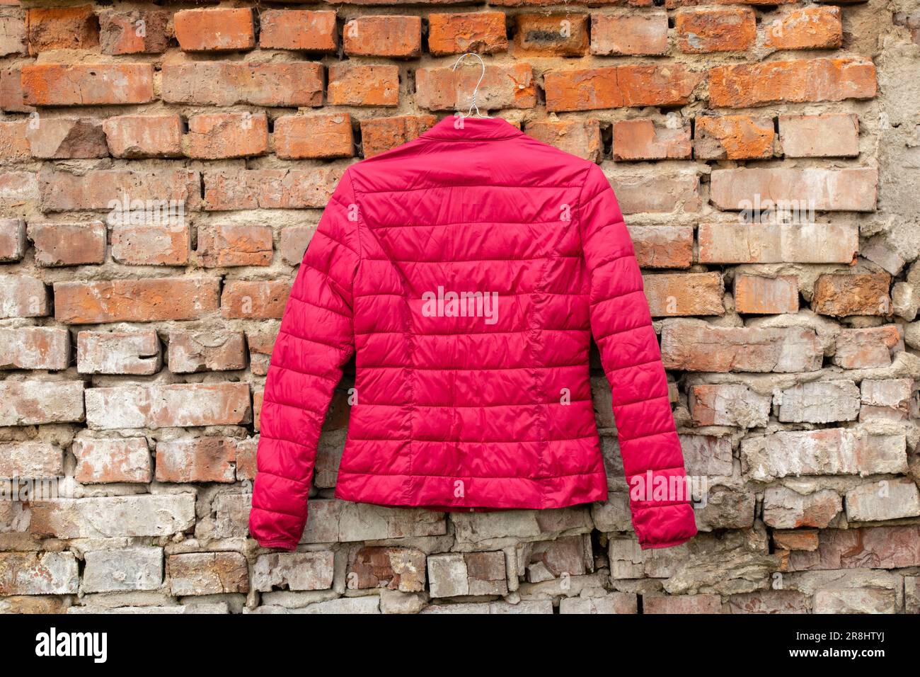 la giacca rossa da donna pesa sugli appendiabiti sulla parete di casa per strada, la moda della giacca da donna Foto Stock