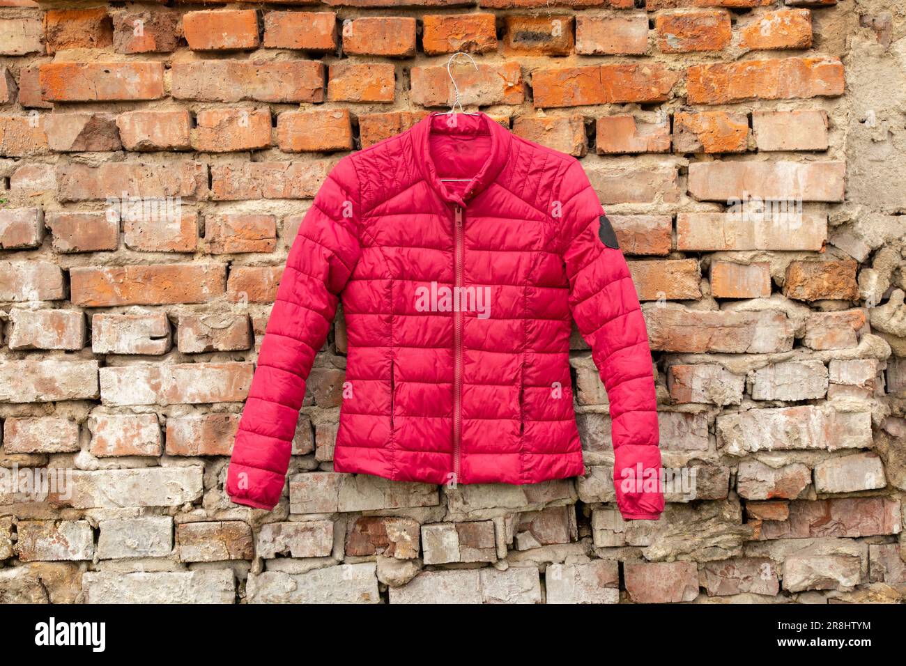 la giacca rossa da donna pesa sugli appendiabiti sulla parete di casa per strada, la moda della giacca da donna Foto Stock