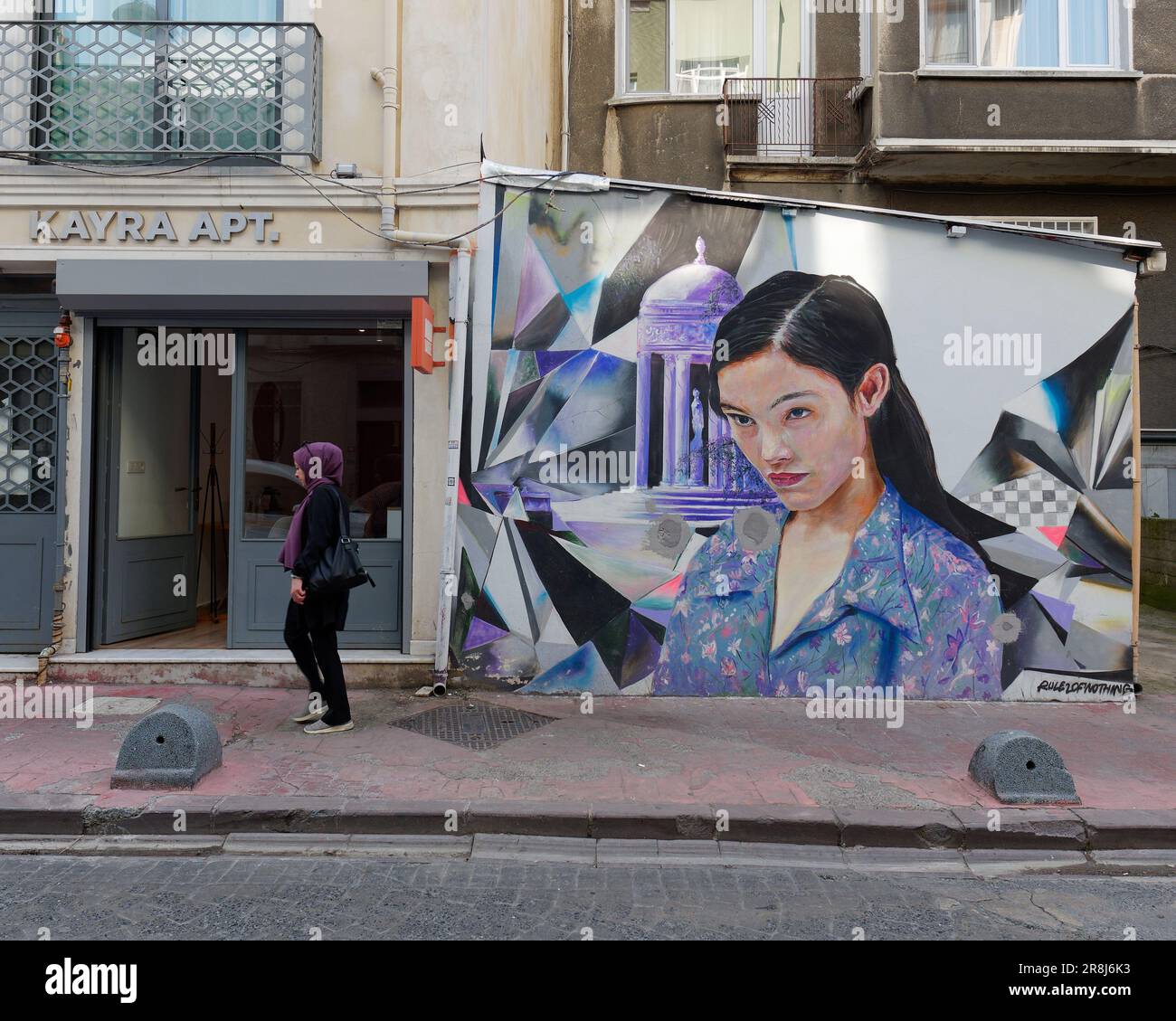 Una donna che indossa un hijab cammina lungo una strada davanti a opere d'arte, mentre dipinge una donna in una camicetta blu. Istanbul, Turchia Foto Stock