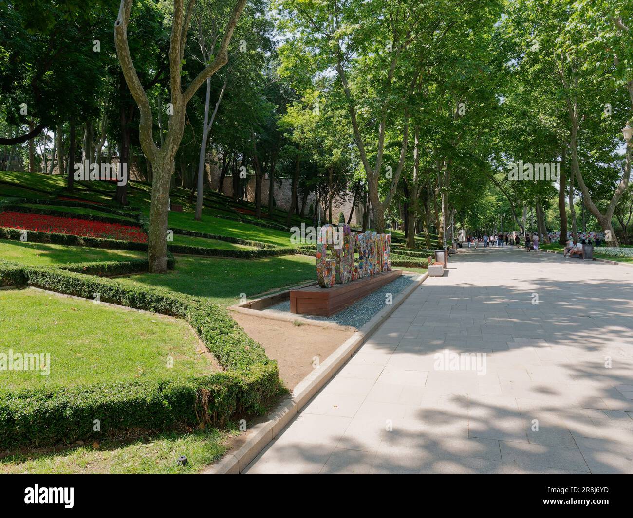 Insegna di Gulhane dipinta con fiori all'interno del parco di Gulhane a Istanbul, Turchia. la gente si siede sulle panchine all'ombra del sole estivo. Foto Stock