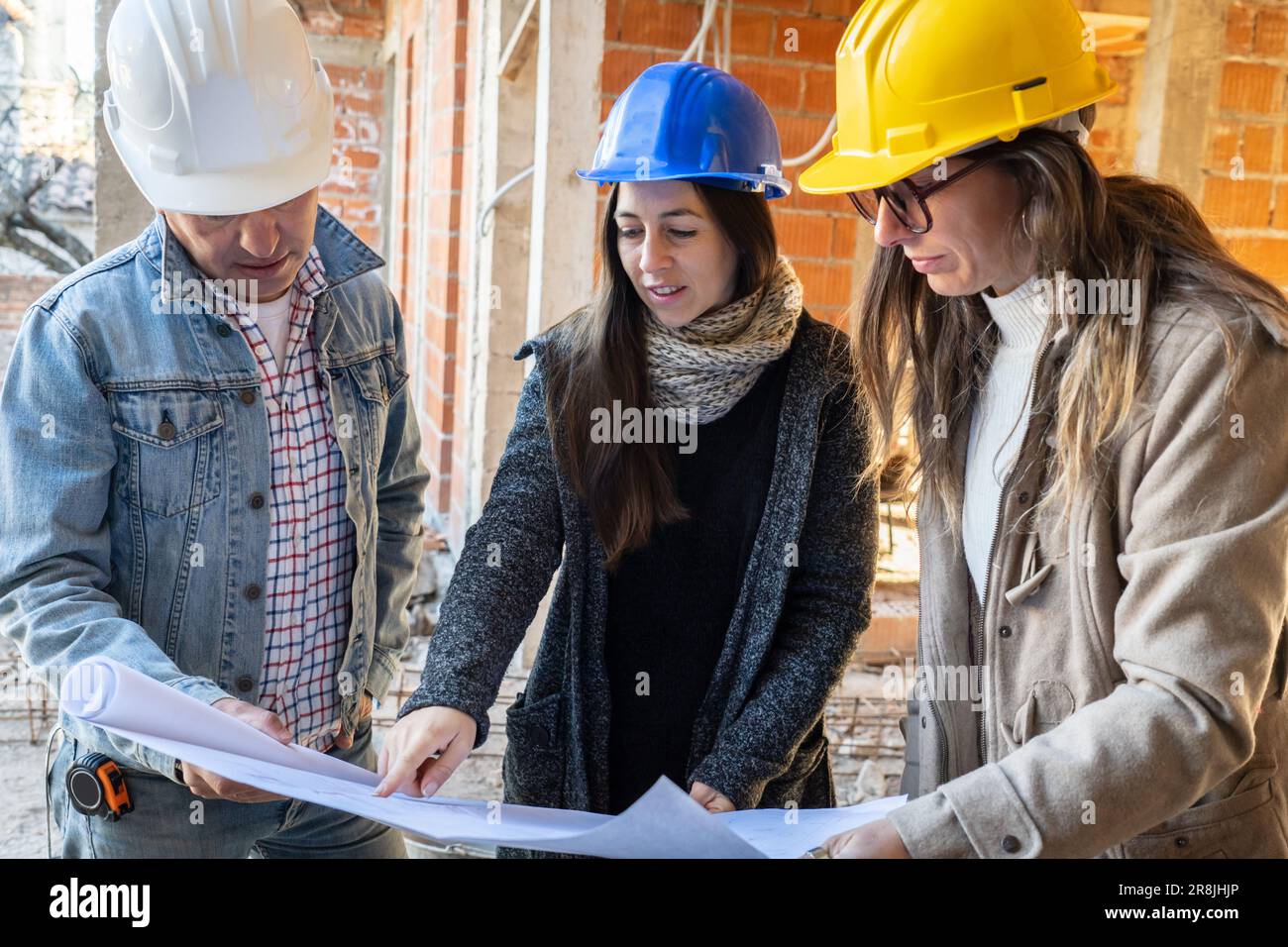 Un ingegnere latino e un team di architetti femminili con un progetto di costruzione in corso. Responsabile e ingegnere della costruzione che lavora in un cantiere Foto Stock