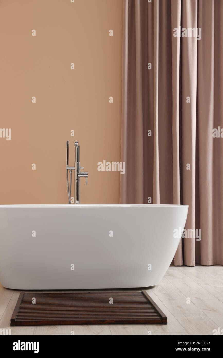 Elegante bagno interno con vasca in ceramica vicino a tende beige Foto Stock