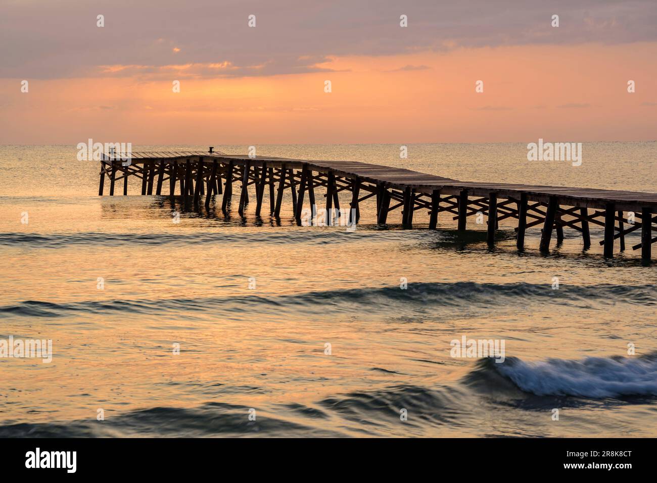 Alba estiva su un molo di legno su una spiaggia di Platja de muro (Maiorca, Isole Baleari, Spagna). Esempio: Amanecer veraniego en un muelle de madera en muro Foto Stock