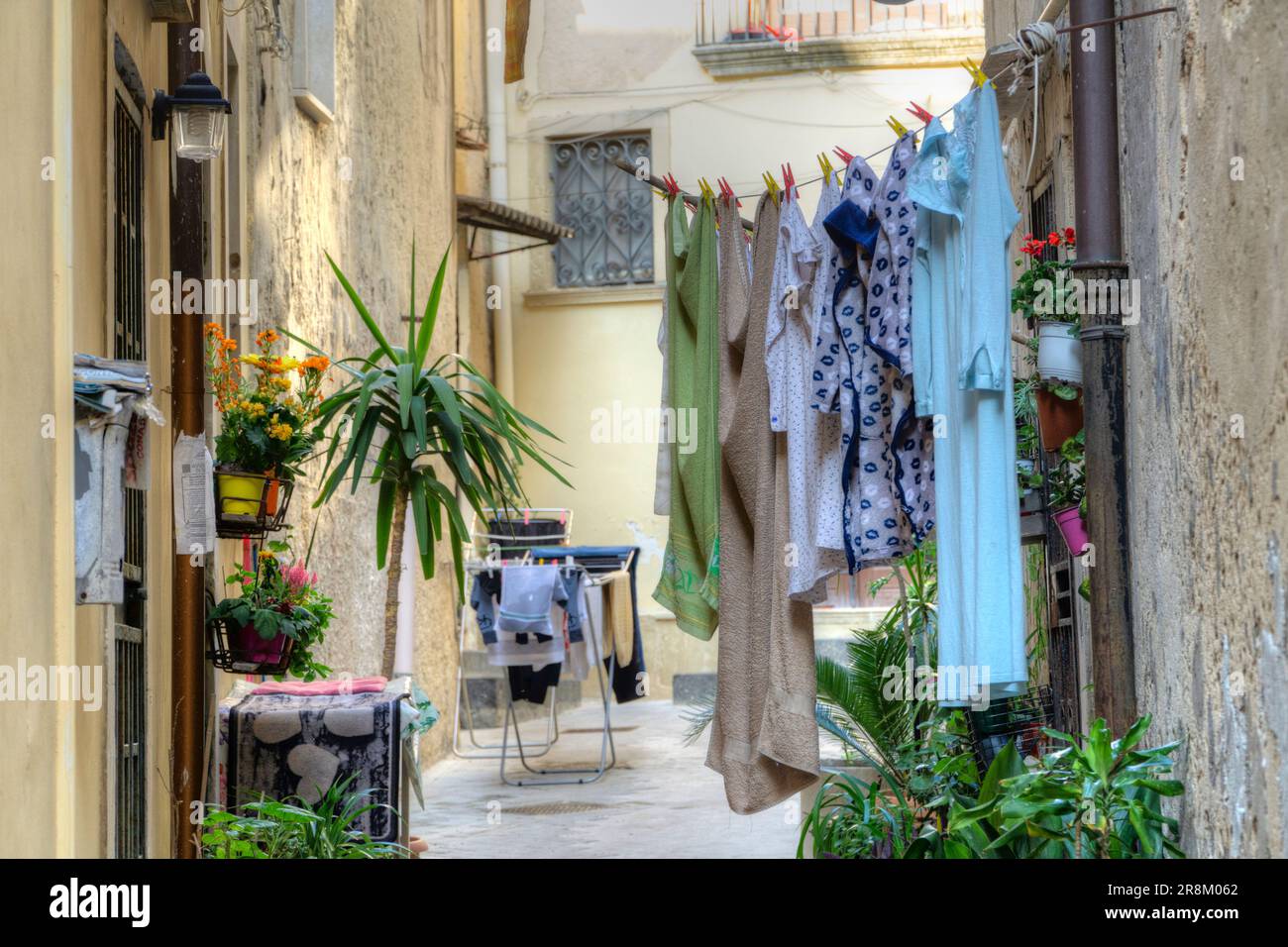 I vestiti lavati in arenaria dorata gialla del cortile dell'isola di Ortigia si asciugano on line e le piante in vaso Foto Stock