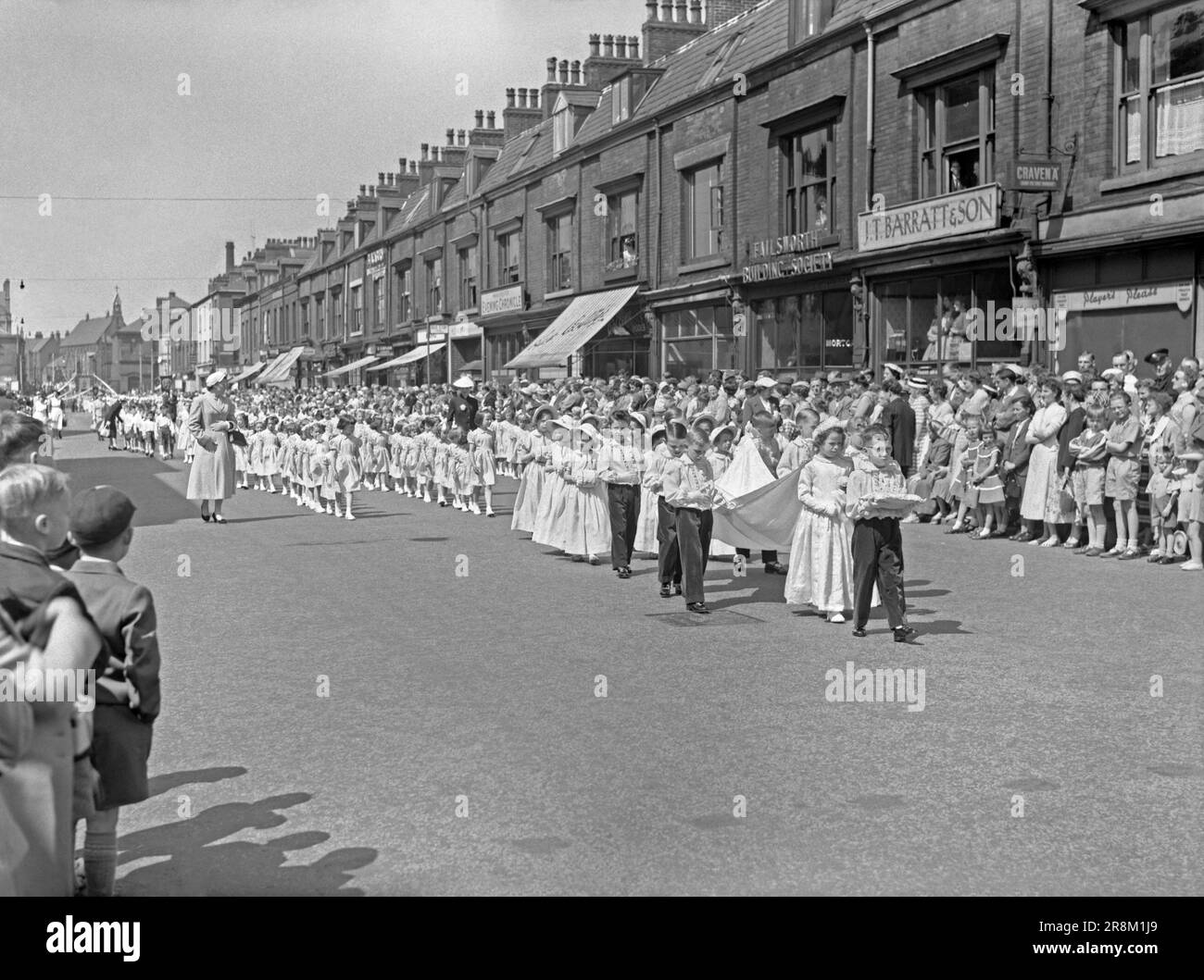 Una processione Whit Walks a Union Street, Oldham, Greater Manchester, Lancashire, Inghilterra, Regno Unito c.1960. Qui i bambini sono al centro della sfilata con le ragazze che indossano i cofani. Una ‘regina’ con una ragazza che porta la sua corona è sul davanti. L'evento religioso della Chiesa d'Inghilterra si svolse tradizionalmente il venerdì di Whit, con bambini fortemente coinvolti insieme a bande d'ottone e d'argento. Manchester aveva la più grande Whit Walks, ma altre Whit Walks erano popolari soprattutto nel nord-ovest dell'Inghilterra. Whit Walks a Manchester ora si svolge durante il Spring Bank Holiday Monday, una fotografia d'epoca degli anni '1950/'60. Foto Stock