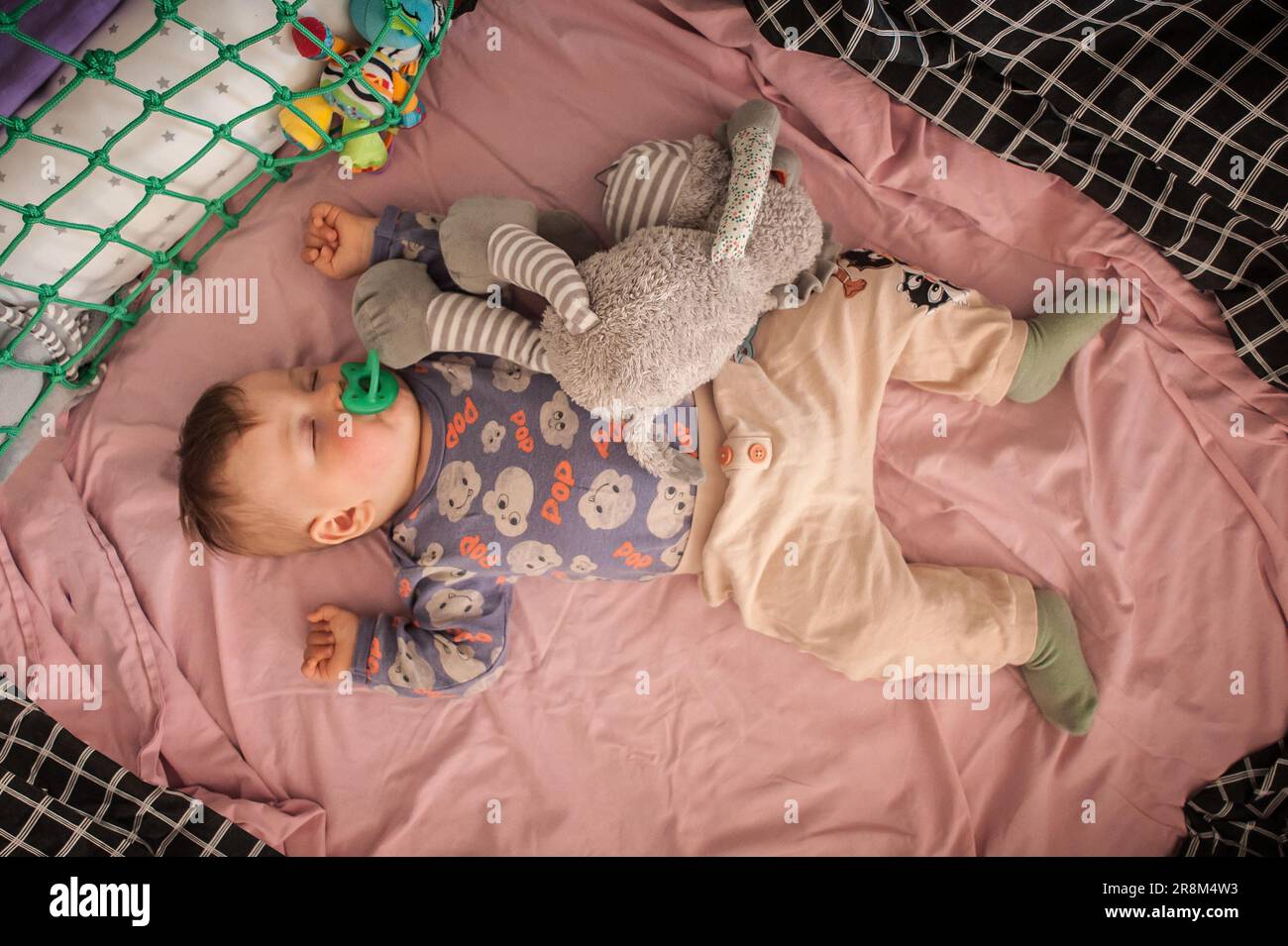 Un bambino grazioso sta dormendo pacificamente e si rilassa sul suo letto con i giocattoli. Vista dall'alto della culla. Amore ed emozioni familiari Foto Stock