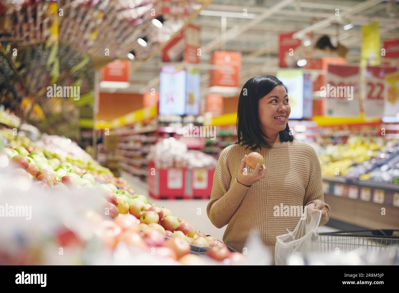 Donna sorridente in piedi nel supermercato e con in mano la mela Foto Stock