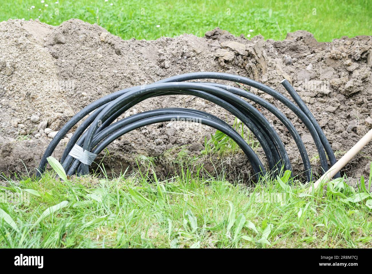 Cavo di alimentazione nero avvolto in una stretta fossa nel prato per installare una connessione casa, concetto di energia, spazio copia, fuoco selezionato Foto Stock