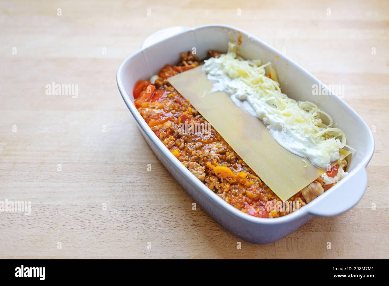 Cottura di lasagne, strati di salsa bolognese, fogli piatti di pasta, crema o bechamel e formaggio in una casseruola su un tavolo da cucina in legno, spazio copia, Foto Stock