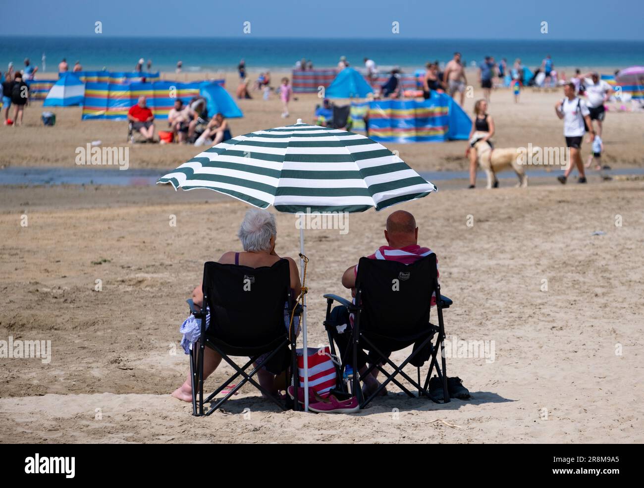 I turisti potranno godersi il sole sulla spiaggia di Peranporth, Cornovaglia, Inghilterra. I frangivento multicolore e gli ombrelli proteggono dal calore. Foto Stock