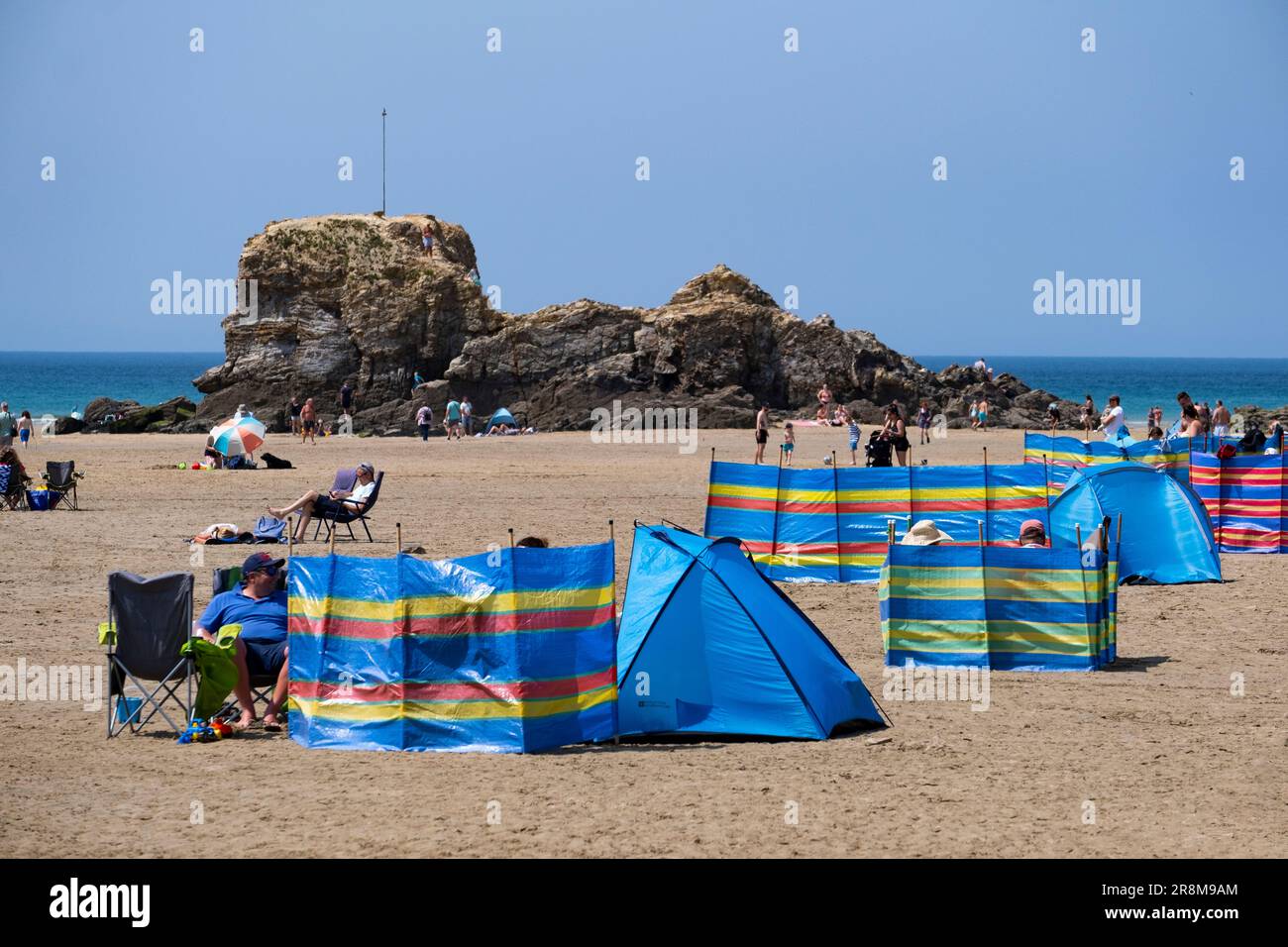I turisti potranno godersi il sole sulla spiaggia di Peranporth, Cornovaglia, Inghilterra. I frangivento multicolore e gli ombrelli proteggono dal calore. Foto Stock