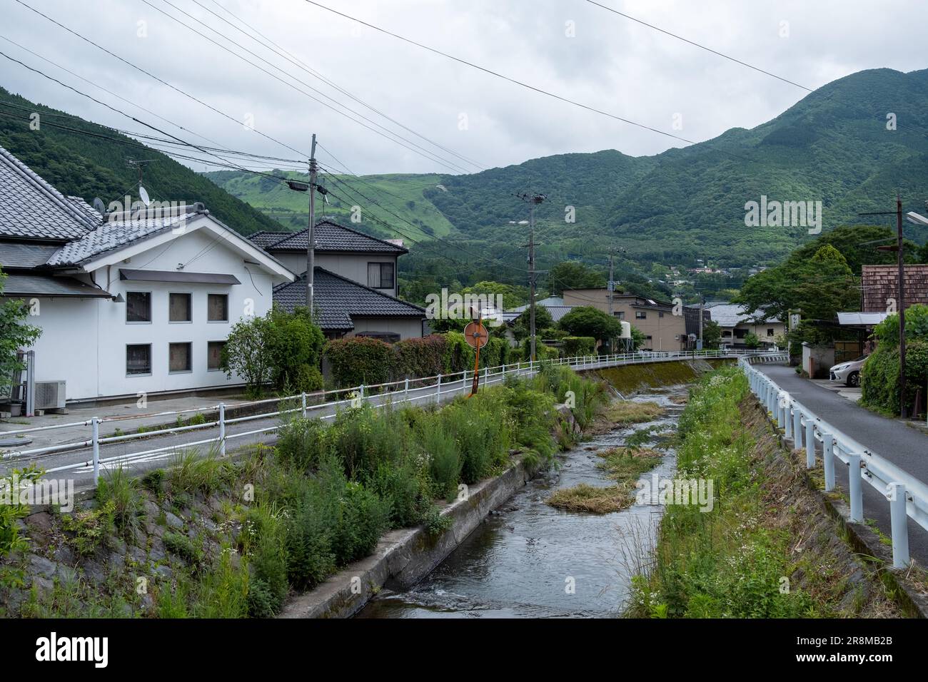 Campagna giapponese con canale che attraversa il villaggio e montagne sullo sfondo scattate a Yufuin, Oita, Giappone. Foto Stock