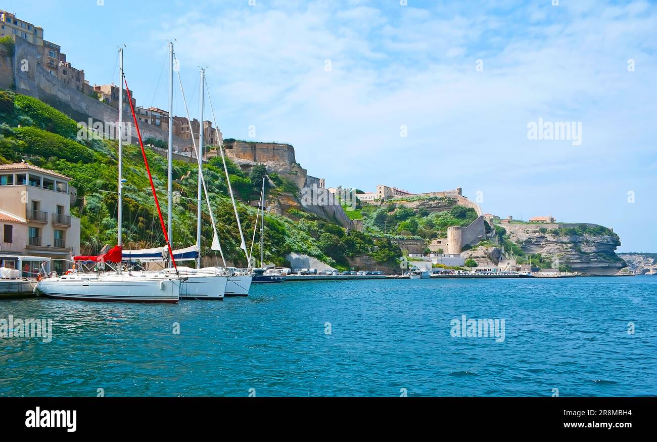 La gita in mare lungo il porto di Bonifacio con vista sugli yacht a vela ormeggiati e sulle scogliere calcaree, sormontate da bastioni storici e torri del Foto Stock