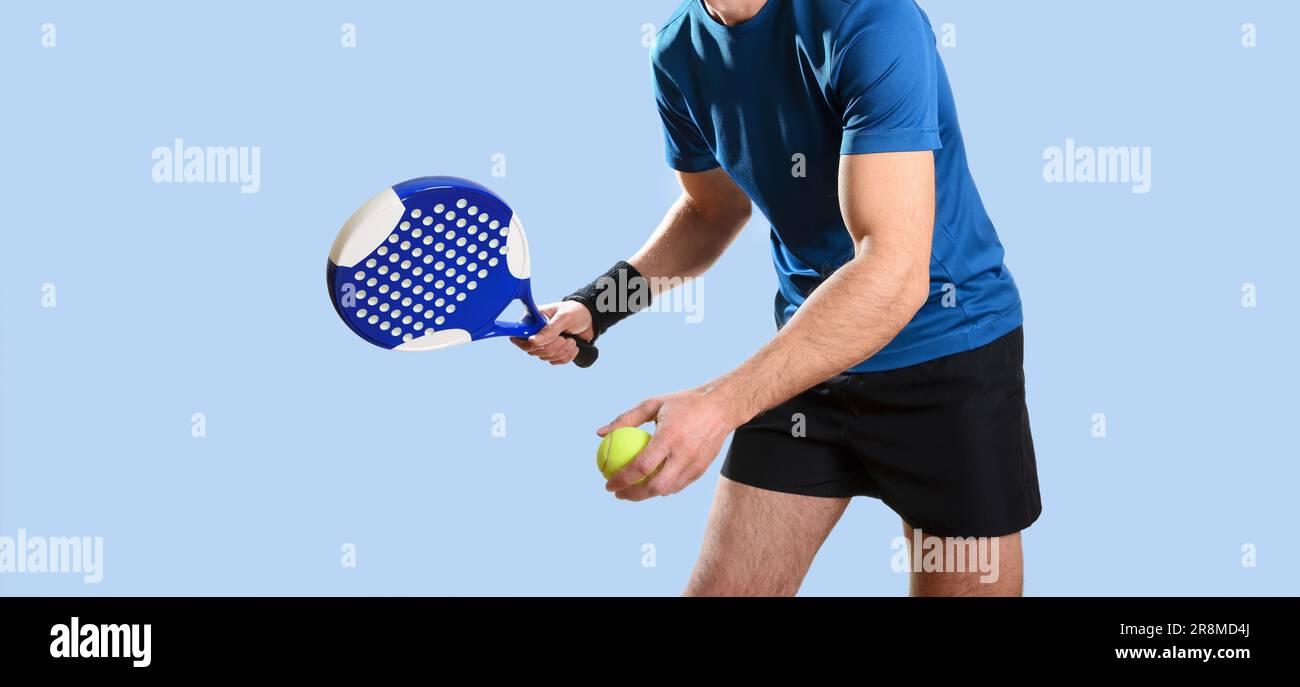 Dettaglio ritratto del giocatore padel dotato di abbigliamento sportivo con gesto di esecuzione di un servizio con sfondo blu isolato. Vista frontale. Foto Stock