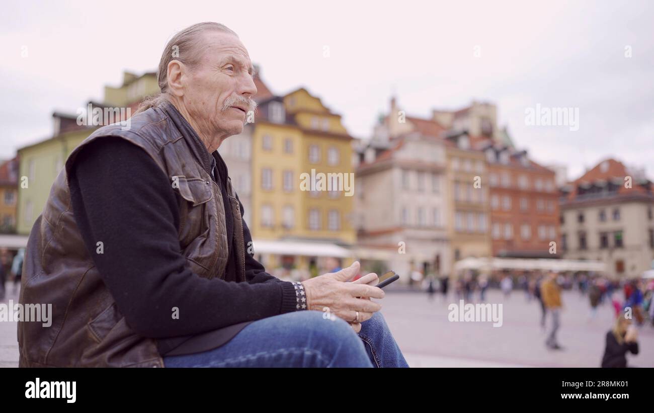 Senior siede sui gradini e visita turistica tenendo in mano uno smartphone nel centro storico di una vecchia città europea. Piazza del Palazzo, centro storico di Varsavia Foto Stock