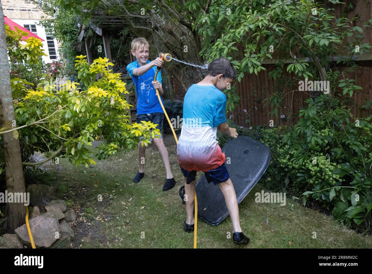 I ragazzi che hanno una lotta per l'acqua utilizzando un tubo flessibile nel loro giardino residenziale nel sud-ovest di Londra, Inghilterra, Regno Unito Foto Stock