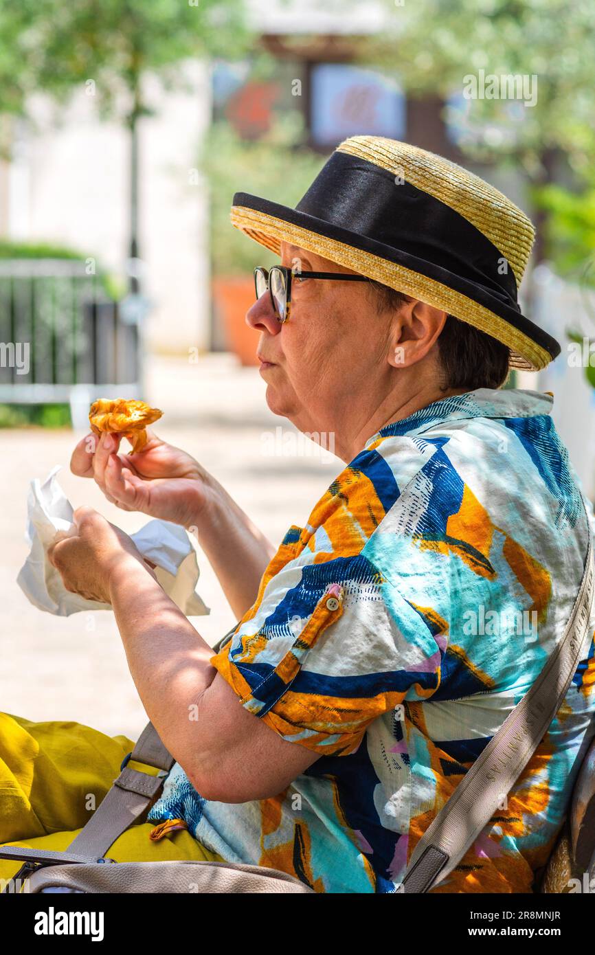 Donna anziana matura in cappello di paglia sul centro città panca giardino mangiare un dolce - Tours, Indre-et-Loire (37), Francia. Foto Stock