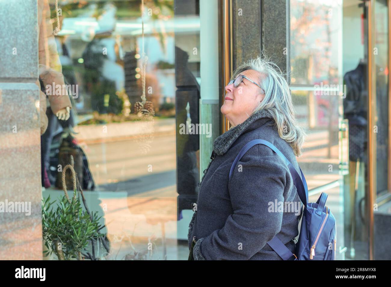 Ronda, malaga, spagna donna più anziana in capelli bianchi e cappotto con borse per la spesa in una vetrina Foto Stock