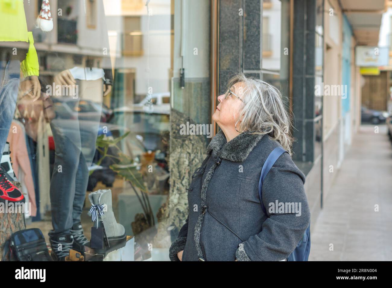 Ronda, malaga, spagna donna più anziana in capelli bianchi e cappotto con borse per la spesa in una vetrina Foto Stock