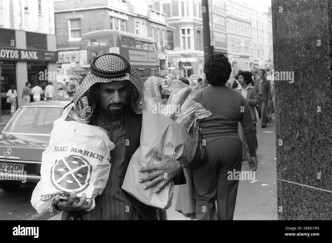 Poveri arabi a Londra Shopping per la drogheria. Durante la fine degli anni '1970s i governi del Medio Oriente hanno fornito assistenza sanitaria ai loro cittadini a Londra, molti sono stati in alloggi a buon mercato nella zona di Earls Court. Un uomo arabo effettua due borse di shopping di generi alimentari. Earls Court, Londra, Inghilterra circa 1977 70s Regno Unito HOMER SYKES Foto Stock
