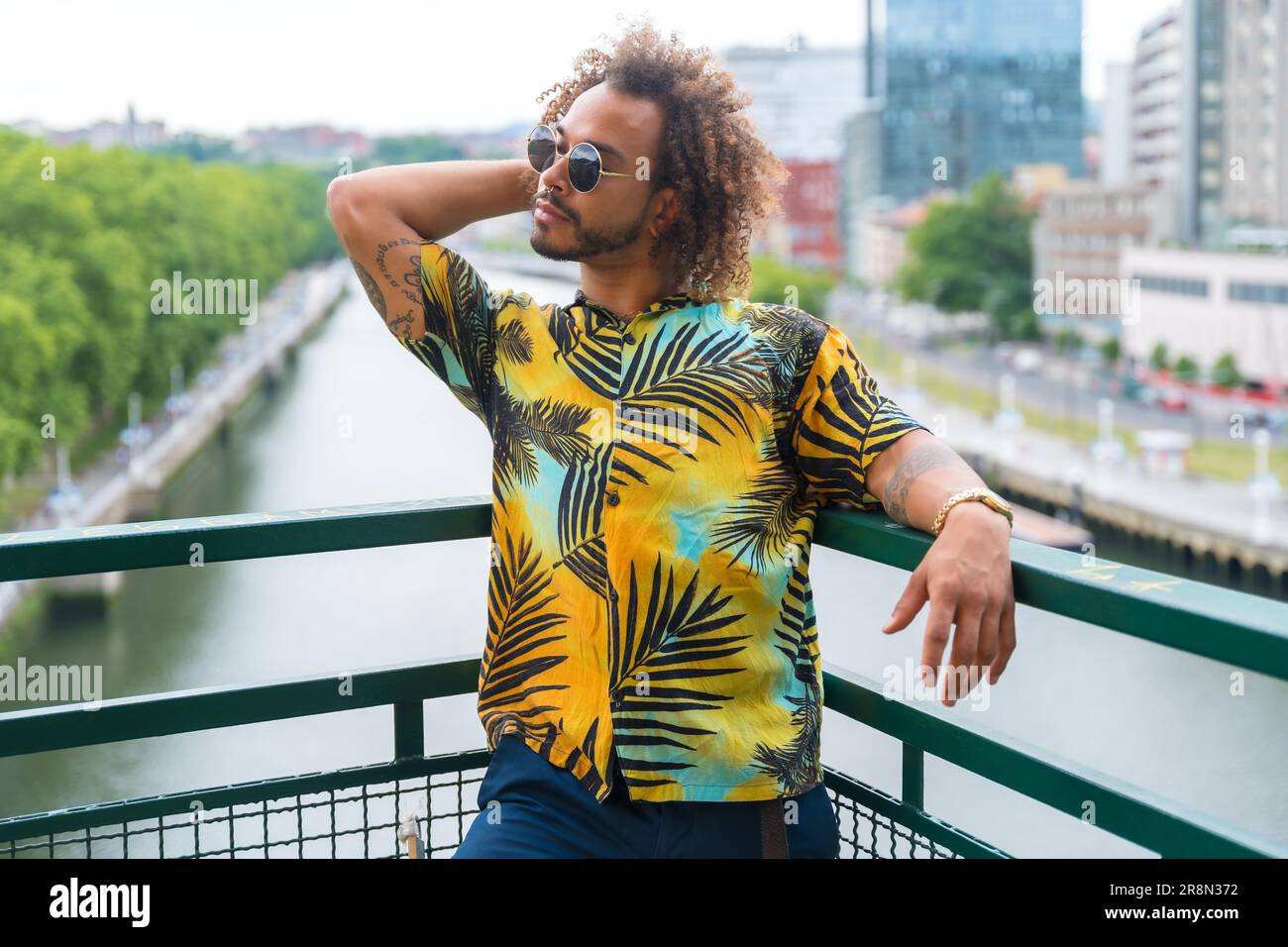 Passato di un uomo attraente con capelli afro in estate indossando una camicia di palma e la città sullo sfondo, godendo la vacanza Foto Stock