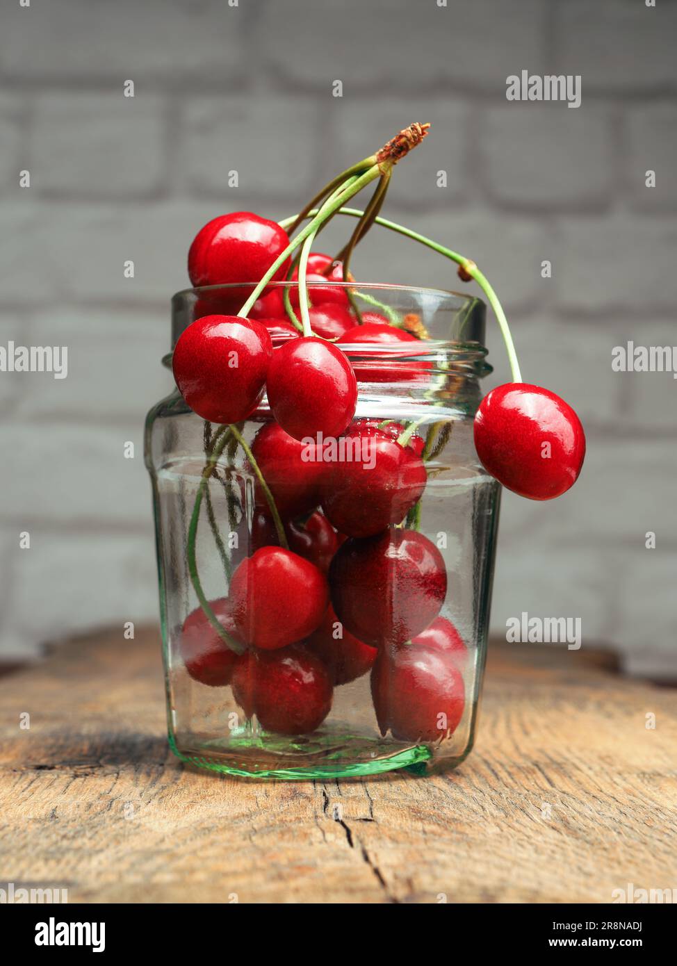 Ciliegie dolci in un vaso di vetro su un tavolo da cucina rustico in legno, cibo sano o concetto di raccolto Foto Stock