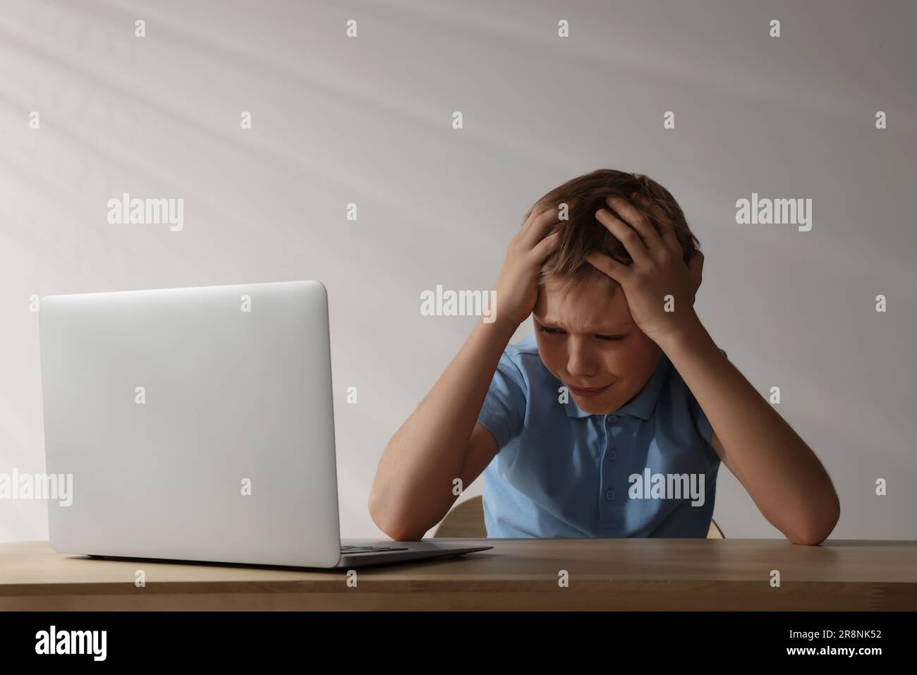 Ragazzo sconvolto con il computer portatile al tavolo di legno. Bullismo informatico Foto Stock